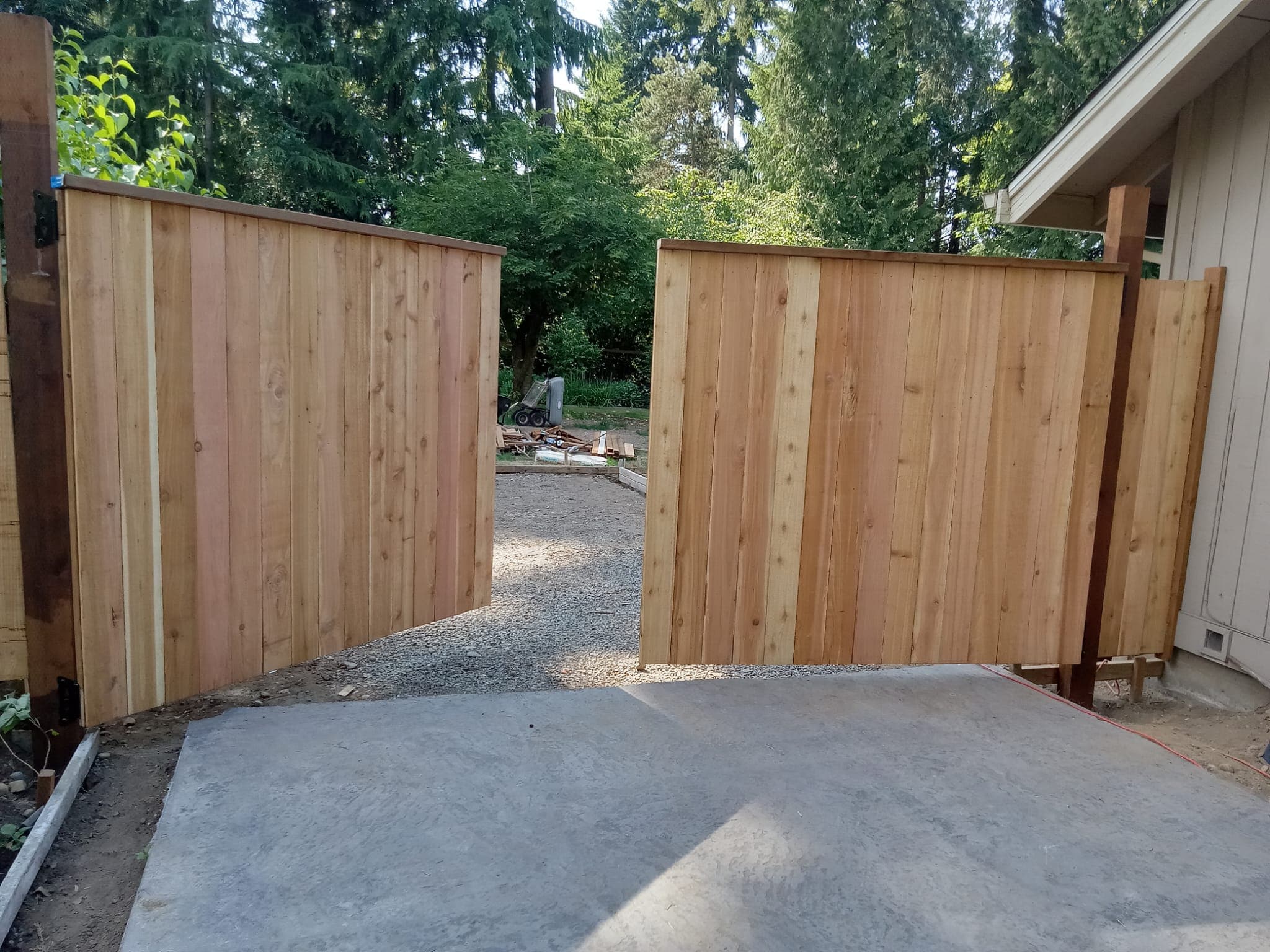 Cedar double gates fully open showing concrete entry pad and gravel pathway